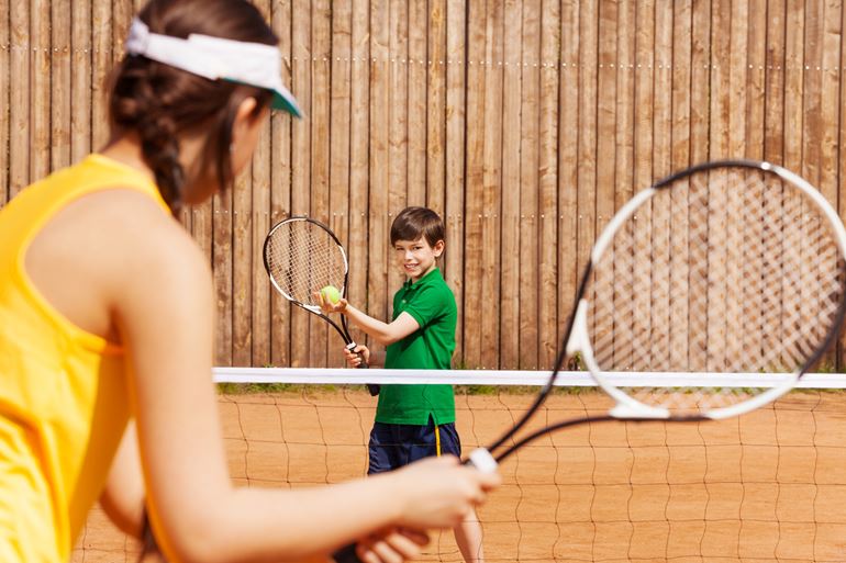 Bilden visar en pojke som spelar tennis med en kvinna
