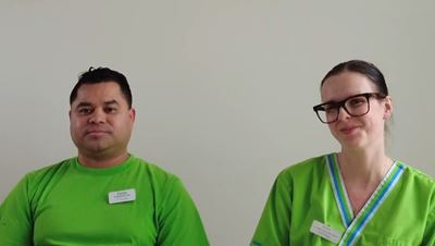 En man i svart hår och en kvinna i brunt uppsatt hår. De har ljusgröna kläder på sig och ler.