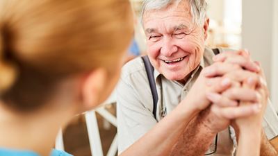 Senior man ler och håller hand med kvinna som sitter med nacken mot kameran.