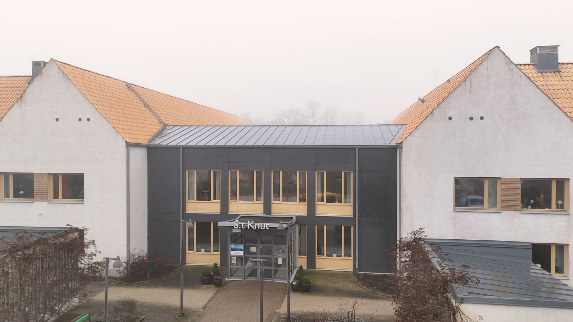 Vitt hus med orange tegeltak i dimmig miljö.