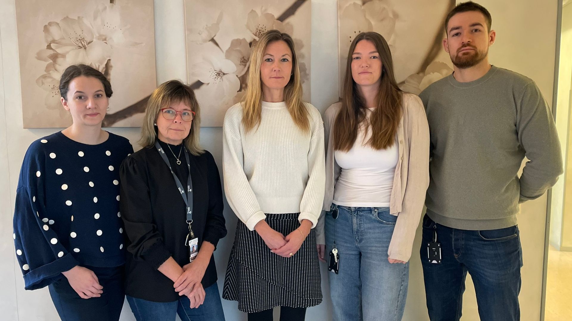 Några av biståndshandläggarna i Vellinge kommun - fyra kvinnor i olika åldrar och en yngre man står framför en vägg med tavlor i beige och rosa.